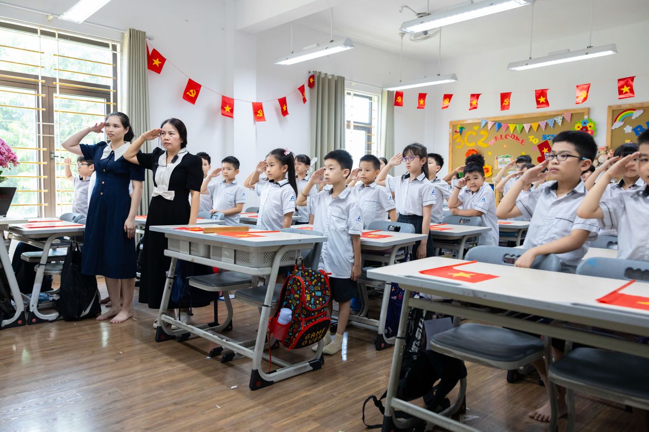 contact-img Children and teachers saluting in a colorful classroom decorated with flags.