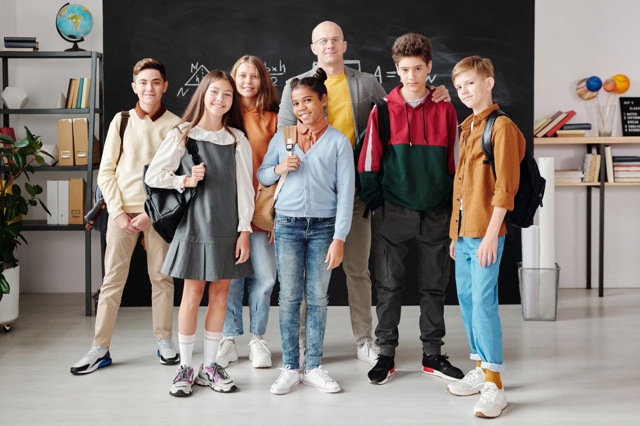 services-01 Group of diverse teenagers posing with their teacher in a modern classroom.