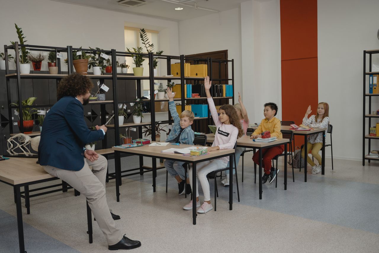 about-01 Students actively participating by raising hands in a modern classroom with attentive teacher and organized environment.