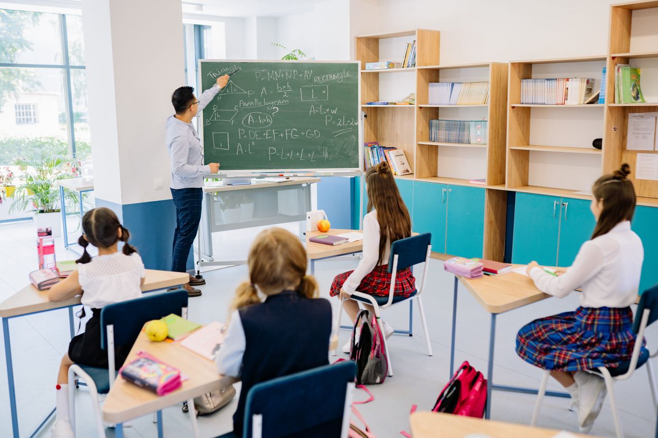 gallery-1 Children in a classroom focused on a math lesson with a teacher. Bright and educational atmosphere.